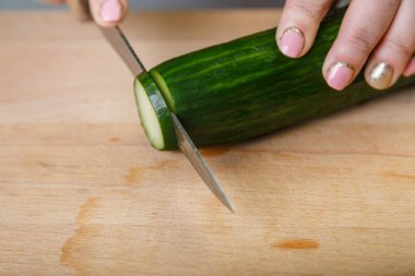 Bir kadın bir salatalık bıçakla keser.