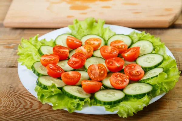 beyaz bir tabağa dilimlenmiş salatalık, domates ve marul yaprakları vardır