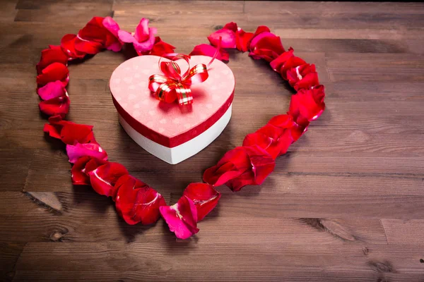 Ahşap masanın üstüne gül lepistas kalp içinde bir hediye bir kalp şeklinde bir kutudur. Kopyalama alanının sağ