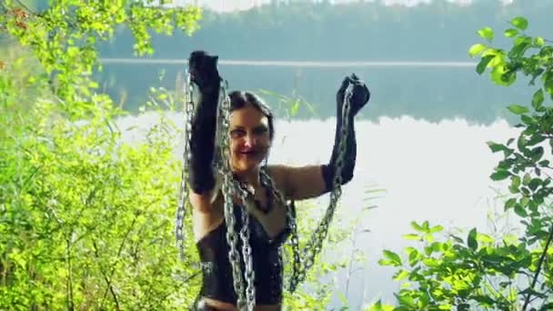 Γέλιο γυναίκα με μια μάγισσα σε μαύρα ρούχα στην όχθη της λίμνης είναι διασκεδάζοντας και Χορεύοντας με αλυσίδες στα χέρια της. Απόκριες. Gothick στυλ. — Αρχείο Βίντεο