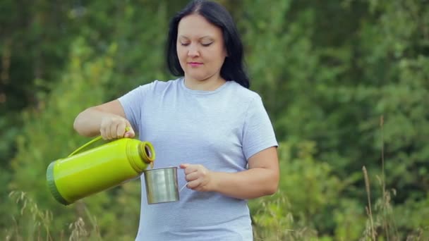 En kvinna resenär i skogen häller varmt te från en termos i en mugg. — Stockvideo