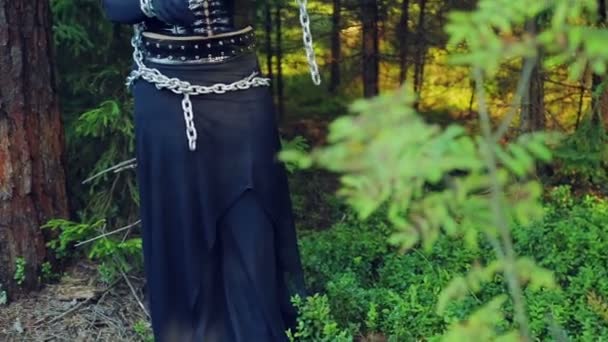 Een vrouw van een heks in zwarte kleding in een forest met kettingen aan een boom gebonden probeert om zichzelf vrij. Halloween. Gothick stijl. — Stockvideo