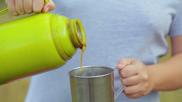The womans hands pour hot tea from the thermos into the mug.