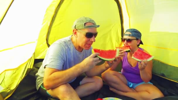 A young woman in a clearing near the tent sits next to a watermelon holding a knife. — Stock Video