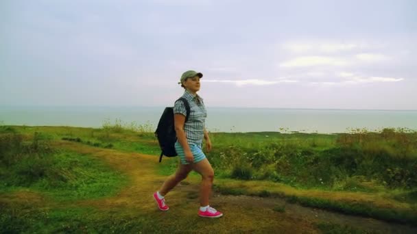 Una mujer con una mochila a sus espaldas caminando por el sendero de la montaña . — Vídeos de Stock