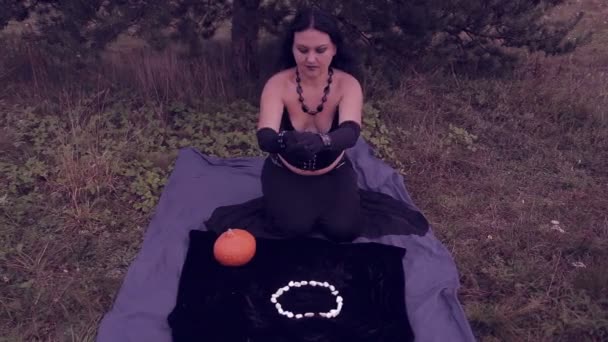Une jeune sorcière en noir jette des cailloux blancs et lit un sort. Halloween . — Video