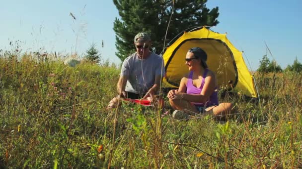 Un homme et une femme près d'une tente touristique dans la forêt coupent une pastèque . — Video