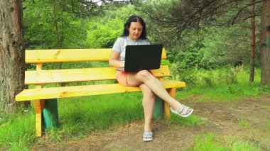 Genç kadın parkta bankta laptop ile çalışma.