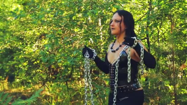 A woman of a witch in black clothes with a chain in her hands in the forest on a bright day. Halloween. — Stock Video