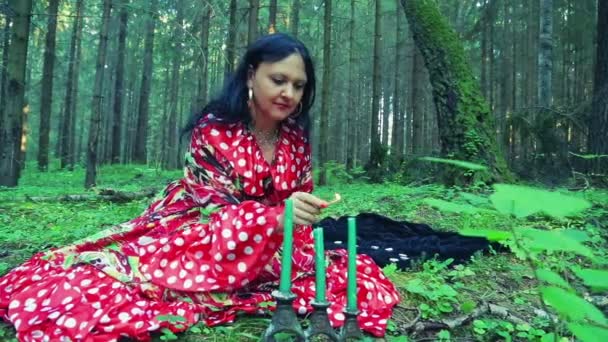 Een jonge zigeuner vrouw licht kaarsen in het bos. — Stockvideo