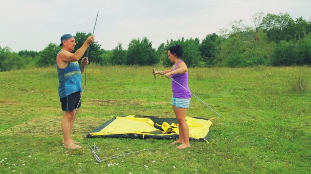 Un homme et une femme ramassent des arcs pour monter une tente . — Video