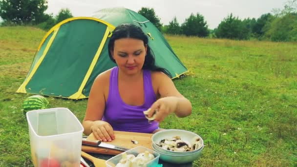 Une femme près de la tente à une table en bois écarte les champignons hachés pour la soupe sur une assiette . — Video