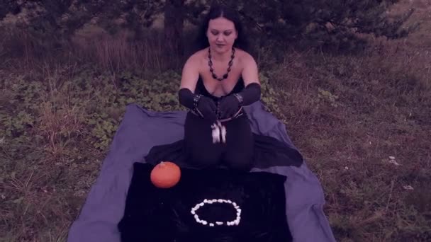 Uma jovem bruxa de preto joga seixos brancos e executa um rito. Halloween. . — Vídeo de Stock