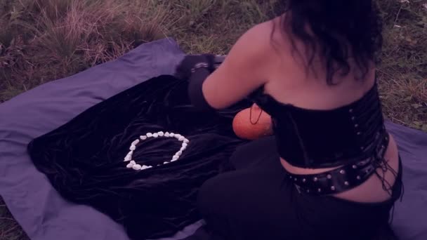 Eine junge Hexe in Schwarz zaubert mit weißen Steinen. Halloween. Ziegenfrisur. — Stockvideo