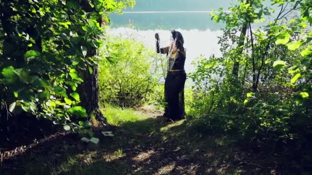 Una donna strega in abiti neri sulla riva del lago si sta divertendo e ballando con le catene in mano. Halloween. Stile Gothick . — Video Stock