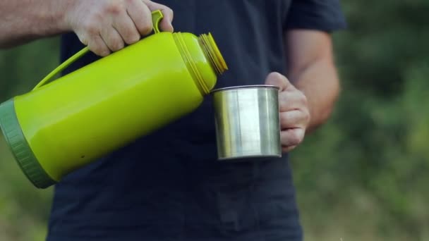 Mens handen giet hete thee uit een thermos in een mok. — Stockvideo
