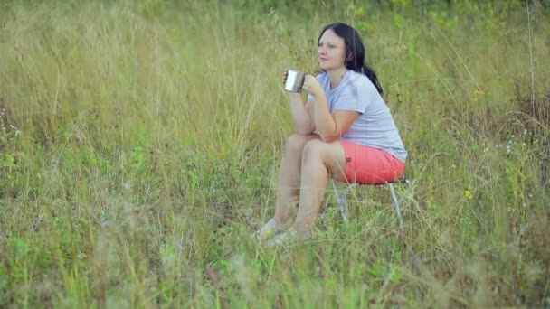 Junge Frau sitzt auf einer Waldlichtung und trinkt Tee. — Stockvideo