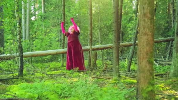 Une jeune sorcière en rouge dans la forêt effectue des actions rituelles avec un personnel . — Video