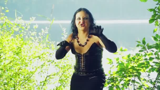 Μια μάγισσα σε μαύρα ρούχα, δίπλα στη λίμνη με τα συναισθήματα του θυμού στο πρόσωπό της. Απόκριες. Gothick στυλ. — Αρχείο Βίντεο