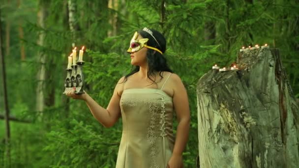 A forest fairy in a golden mask on his face stands at a big stump and holds a candlestick with burning candles in his hand. — Stock Video