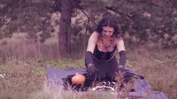 A young sorceress in black conjures over white stones. Halloween. — Stock Video