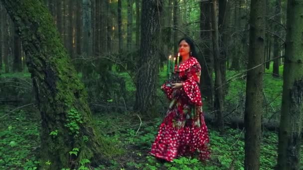 A young gypsy shuvani holds a candlestick with burning candles and looks around in forest thickets. — Stock Video