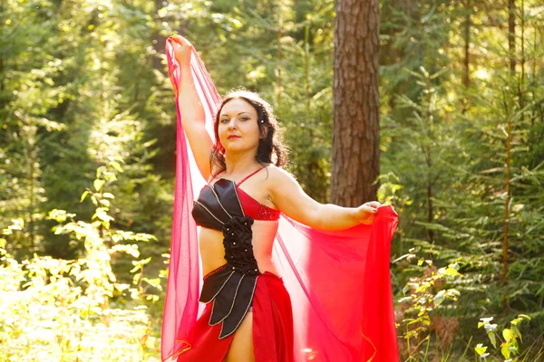 东方舞者穿着红色西装 披着披肩 在森林里阳光明媚的日子里 水平特写 — 图库照片
