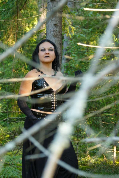 A woman of a witch in black stands in dense forest thickets. Halloween. — Stock Photo, Image