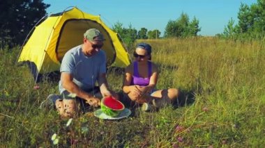 Mutlu bir adam ve kadın ormandaki bir çadır yakın. Bir adam bir karpuz üzerinde büyük boyutta bir bıçakla keser.