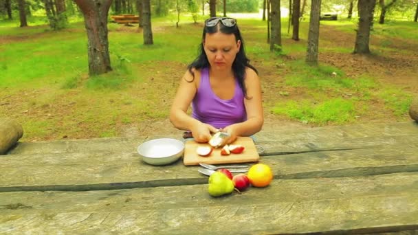 Una giovane donna in un parco a un tavolo di legno cancella la mela dal nucleo . — Video Stock