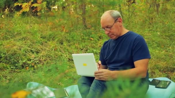 Un hombre con gafas en el borde del bosque con un lápiz en la mano y un portátil encuentra una solución . — Vídeos de Stock
