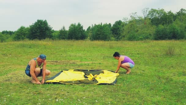 En man och en kvinna sticka pinnar av tältet till marken. — Stockvideo