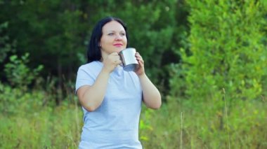 Genç bir kadın çay içme ve doğa hayran orman kenarında duruyor.