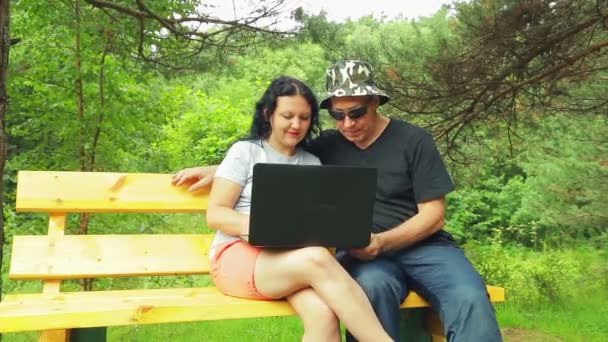 Uomo e donna in parco su panchina che lavorano con il computer portatile . — Video Stock