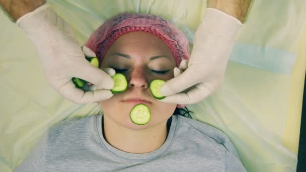As mãos da mulher esteticista são colocadas no rosto de um homem anéis de kiwi de frutas como uma máscara de frutas para o rosto . — Vídeo de Stock