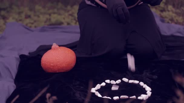 Häxan i svart kastar vita stenar och utför magiska rörelser med händerna. Halloween. — Stockvideo