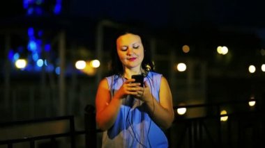 Müzik ve şarkı gece gökyüzü arka planı kulaklık ile sahildeki genç gülümseyen kadın.