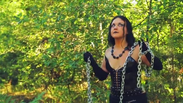 Una mujer de bruja vestida de negro con una cadena en las manos en el bosque en un día brillante. Halloween. Estilo Gothick . — Vídeo de stock