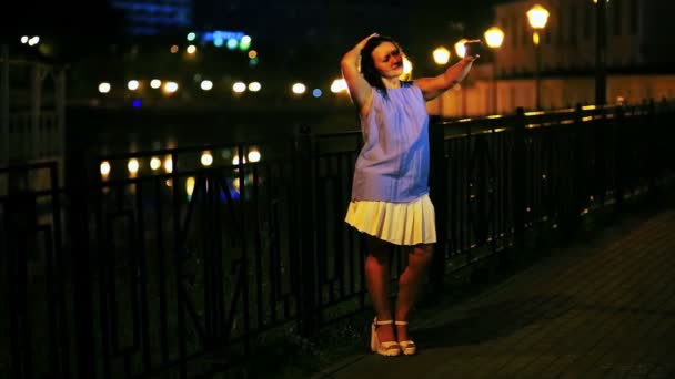 Joven mujer sonriente haciendo selfie en el teléfono móvil en el fondo del muelle y el cielo nocturno . — Vídeo de stock