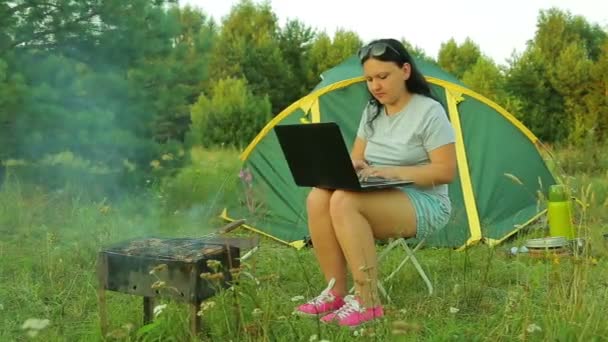 一个男人和一个女人在帐篷附近 一个女人正在用笔记本电脑 一个男人正在烧烤烤肉 — 图库视频影像