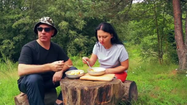 森の端に男と女の観光客倒木の上に座るとフルーツ サラダを食べるし 自然に感心します — ストック動画