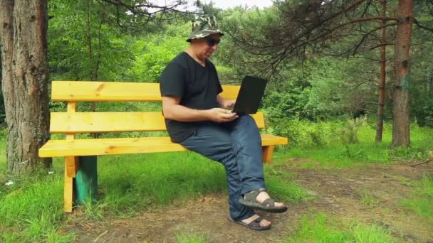 一个戴着太阳镜的人在公园里坐着长凳 和笔记本电脑一起工作 — 图库视频影像