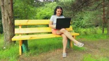 Genç kadın parkta bankta laptop ile çalışma. Dış görev uçan böcekler sürücüler.