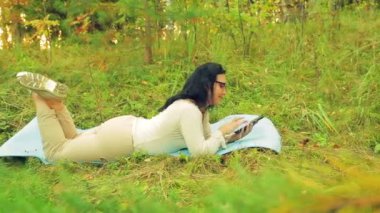 bir tablet ile yoga ve çalışmaları için bir halı üzerinde bir orman içinde bir kadın yatıyor.