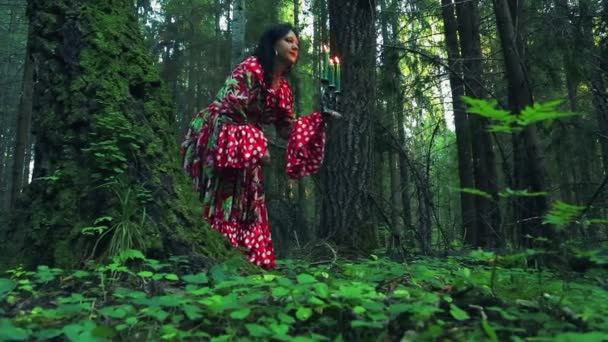 一个年轻的吉普赛人 手里拿着蜡烛 在树林里的一棵大树后面偷看 看着四周 — 图库视频影像
