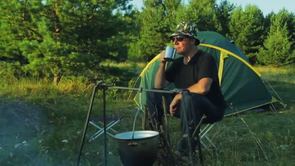 Mannen Solglasögon Sitter Vid Tältet Dricker Och Klockor Plommonstop Hängande — Stockvideo