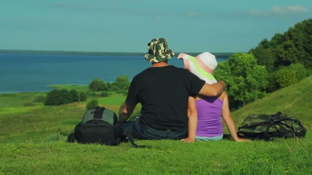 拥抱男人和女人坐在山的边缘 欣赏湖的景色 从后面射击 — 图库视频影像