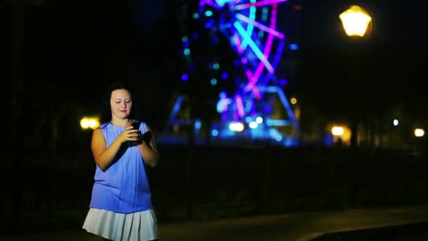 ウォーター フロントの若い女性は 夜の空を背景に携帯電話でメッセージを書き込みます — ストック動画