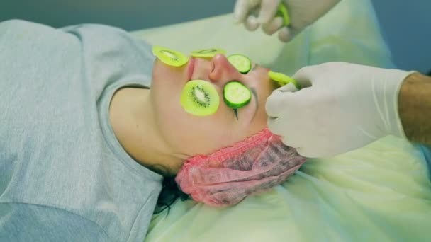 那化妆师的人的手从女人的脸上移除一个来自猕猴桃和黄瓜片的面具 — 图库视频影像