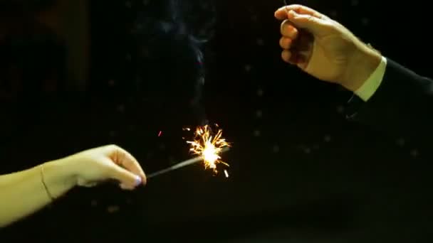 Un hombre y una mujer celebran la Navidad de Año Nuevo con fuegos artificiales de vela de Bengala sobre un fondo negro . — Vídeos de Stock